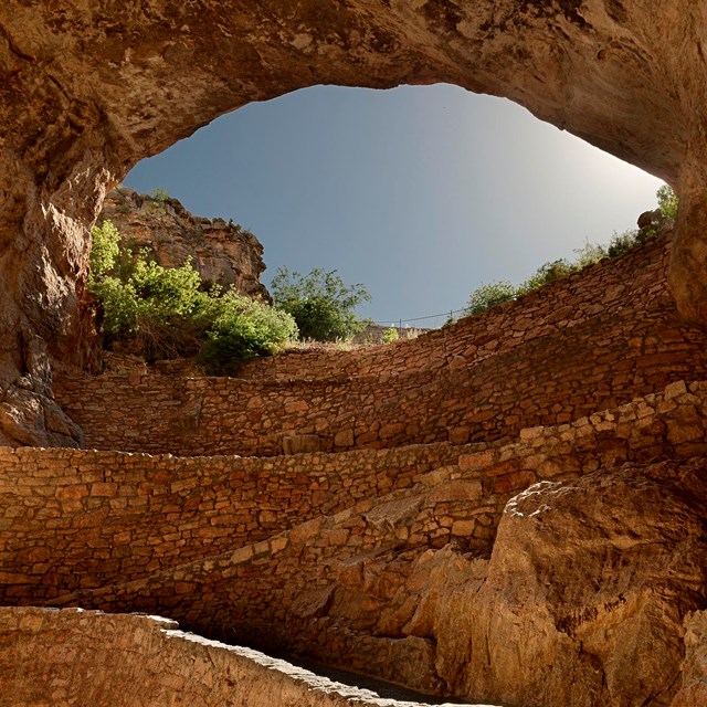 looking up and blue sky through cave opening; cave has tan walls